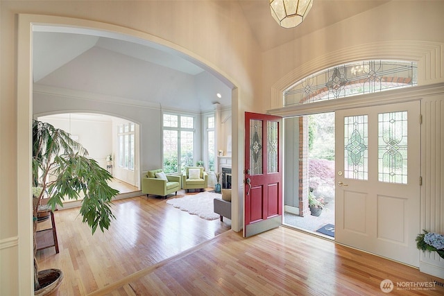 entrance foyer featuring a towering ceiling, arched walkways, wood finished floors, and a fireplace