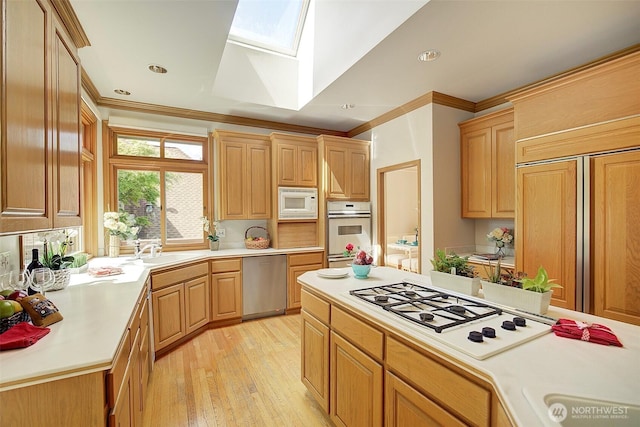 kitchen with a skylight, ornamental molding, white appliances, and a sink