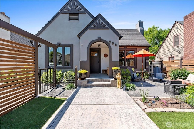 tudor-style house featuring fence, a chimney, and stucco siding