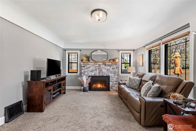 carpeted living room with visible vents, baseboards, and a stone fireplace