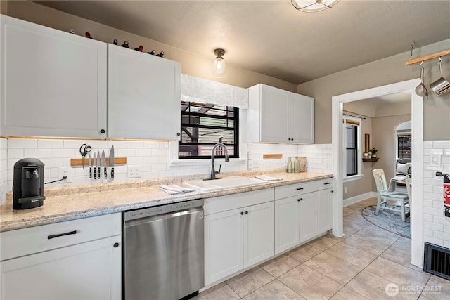 kitchen with decorative backsplash, dishwasher, a sink, light tile patterned floors, and white cabinetry