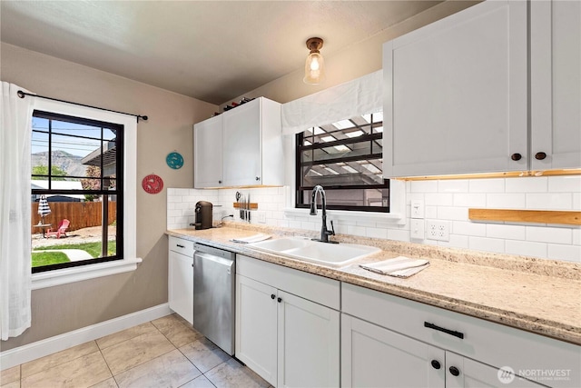 kitchen with tasteful backsplash, stainless steel dishwasher, a sink, baseboards, and white cabinetry