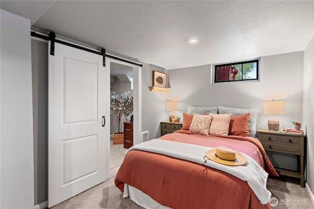 bedroom featuring a textured ceiling, baseboards, a barn door, and light colored carpet