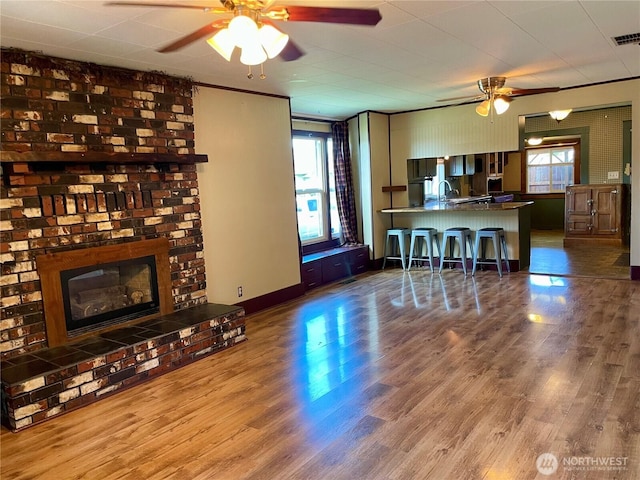 living room with a brick fireplace, ceiling fan, wood finished floors, and a healthy amount of sunlight
