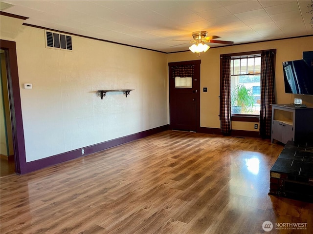 unfurnished living room featuring visible vents, ornamental molding, wood finished floors, baseboards, and ceiling fan