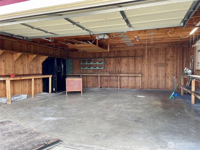 garage featuring wooden walls, a garage door opener, and black fridge with ice dispenser