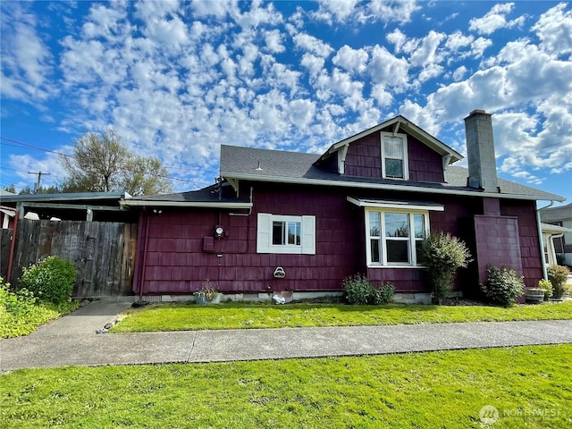 view of front of home with a chimney, roof with shingles, fence, and a front yard