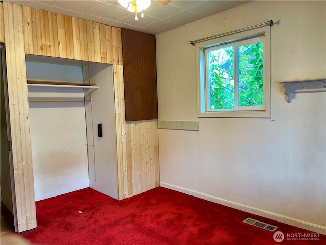 unfurnished bedroom featuring carpet floors, wooden walls, and visible vents