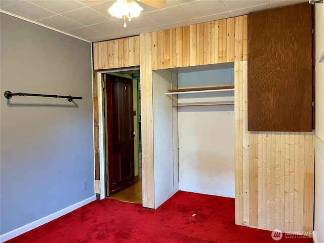unfurnished bedroom with wooden walls, carpet flooring, and a closet