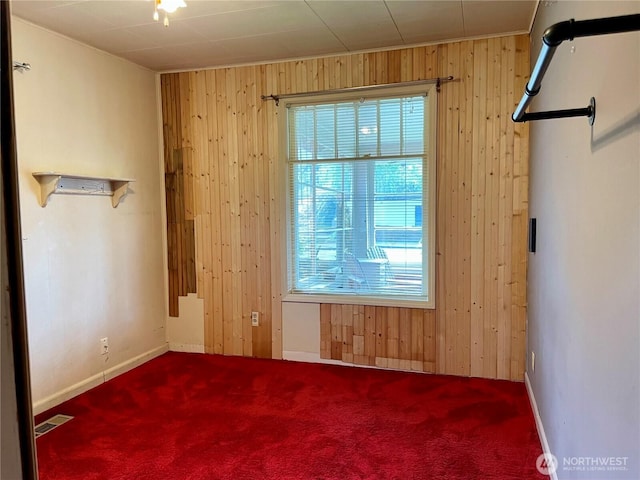 empty room featuring visible vents, carpet, wood walls, and a wealth of natural light