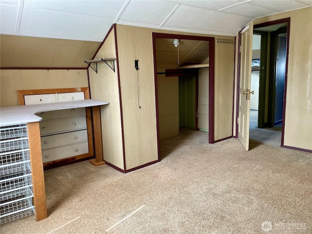 unfurnished bedroom featuring light colored carpet, lofted ceiling, and wooden walls
