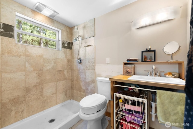 bathroom featuring a sink, a tile shower, toilet, and visible vents