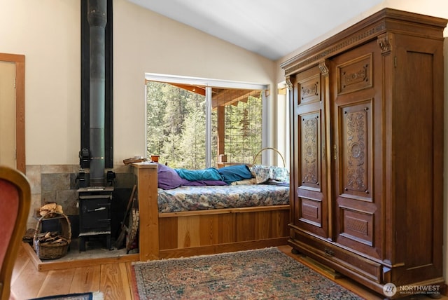 bedroom with a wood stove, wood finished floors, and lofted ceiling