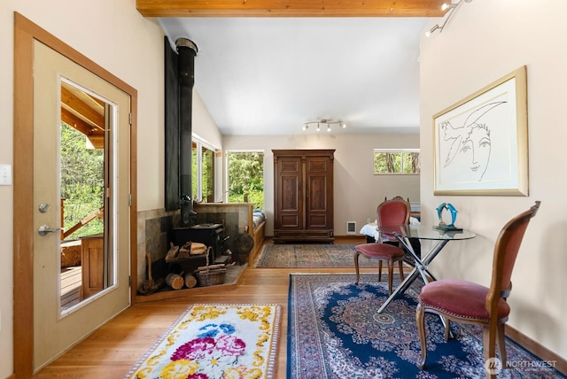 sitting room with a wood stove, rail lighting, vaulted ceiling, light wood-type flooring, and visible vents
