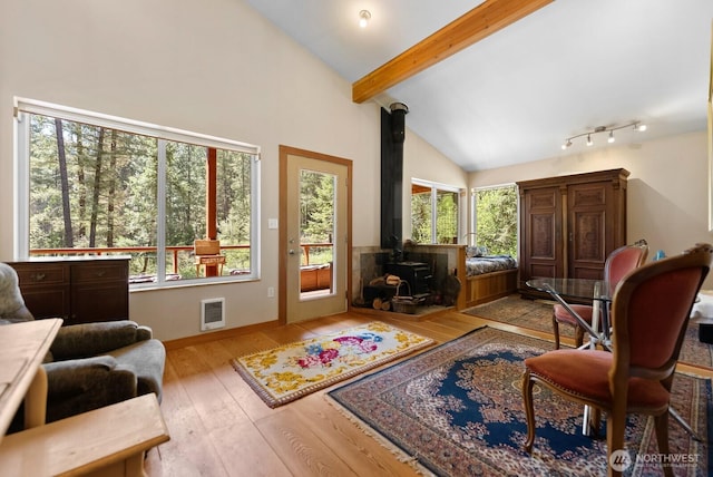 living area with beam ceiling, a wood stove, baseboards, visible vents, and hardwood / wood-style flooring