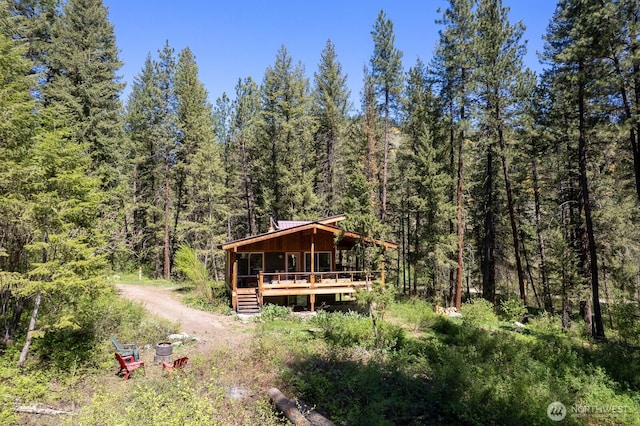 exterior space featuring dirt driveway, a wooded view, and a wooden deck