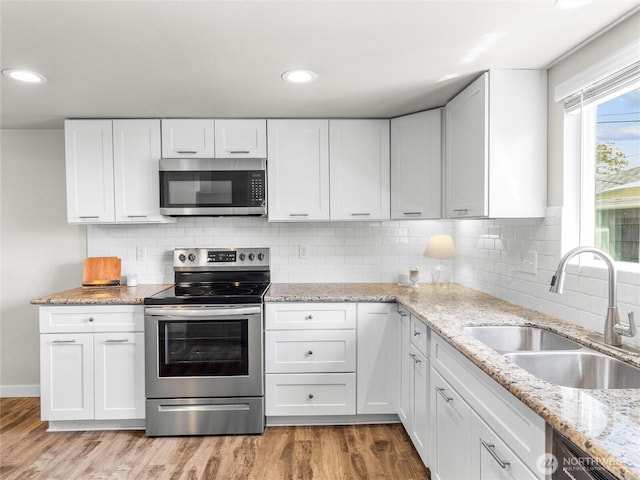 kitchen with stainless steel appliances, a sink, white cabinetry, light wood-style flooring, and recessed lighting