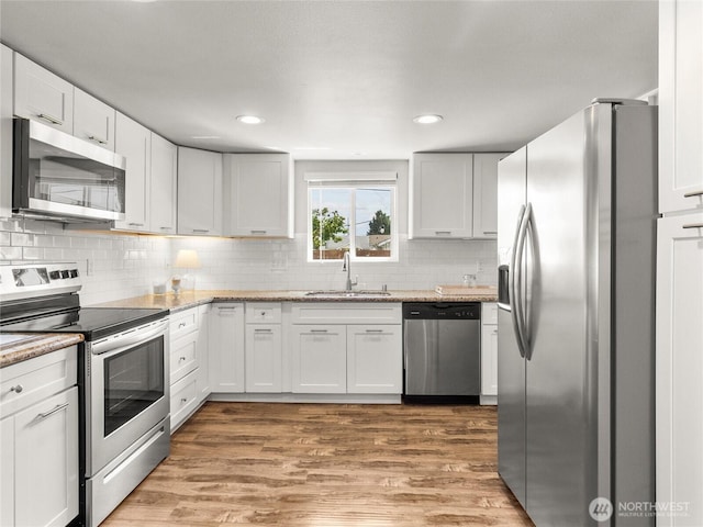 kitchen featuring appliances with stainless steel finishes, a sink, white cabinetry, light wood-type flooring, and backsplash