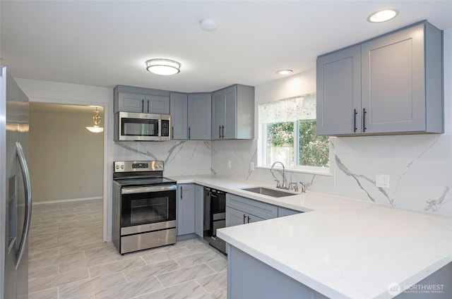 kitchen featuring stainless steel appliances, a sink, gray cabinets, light countertops, and a peninsula