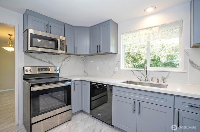 kitchen with appliances with stainless steel finishes, a sink, light countertops, gray cabinetry, and decorative backsplash