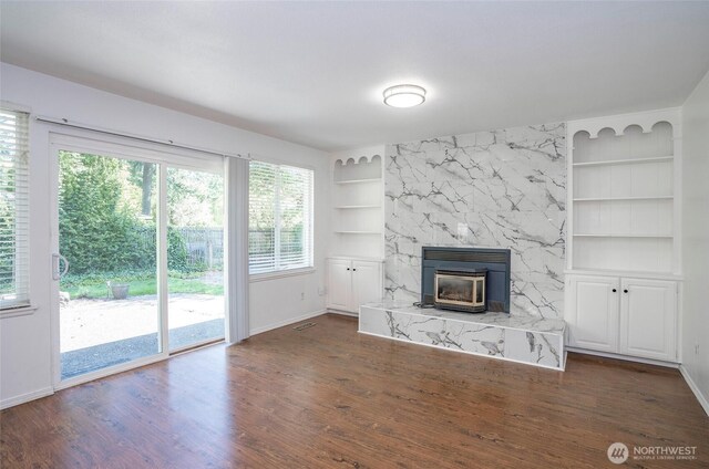 unfurnished living room featuring built in shelves, baseboards, a high end fireplace, and dark wood-type flooring