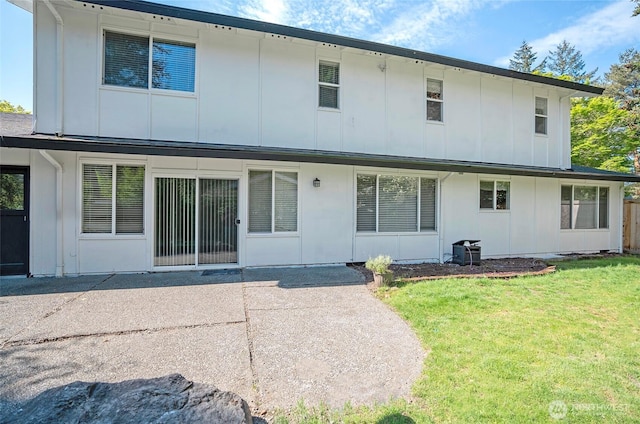 back of property with board and batten siding, a lawn, and a patio area