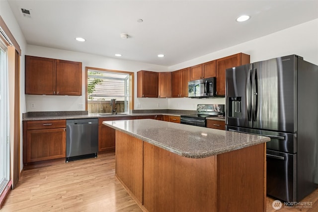 kitchen with stainless steel appliances, a sink, light wood finished floors, a kitchen island, and dark stone countertops