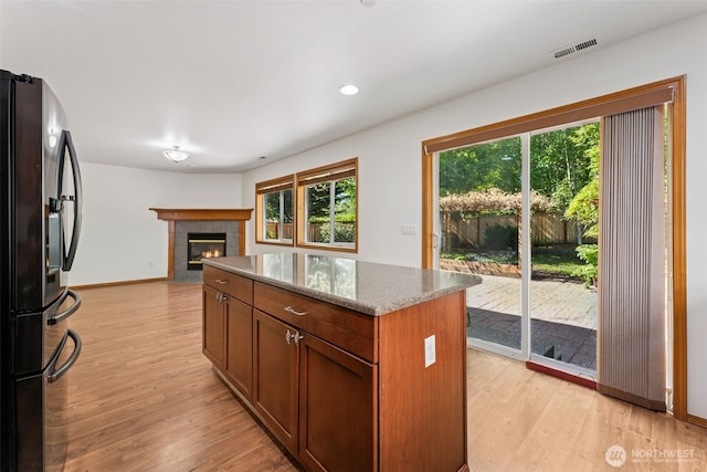 kitchen with stainless steel refrigerator with ice dispenser, light wood-style flooring, a kitchen island, light stone countertops, and recessed lighting