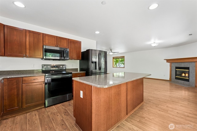 kitchen with black appliances, ceiling fan, light wood-type flooring, a kitchen island, and a tiled fireplace