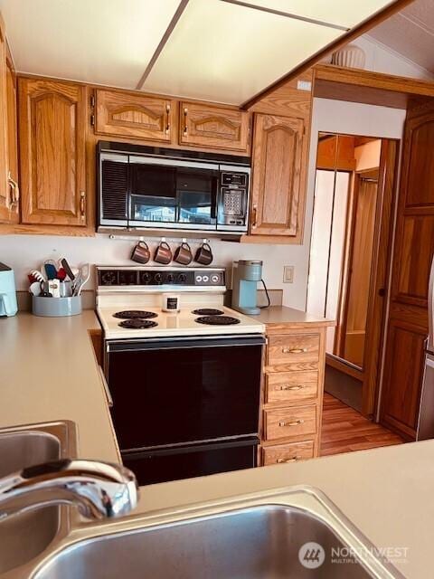 kitchen featuring range with electric stovetop, light countertops, brown cabinetry, and refrigerator