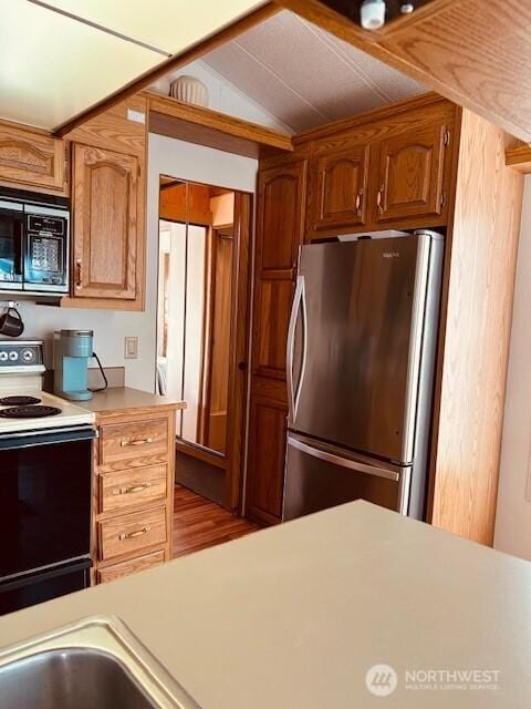 kitchen with freestanding refrigerator, lofted ceiling, light countertops, built in microwave, and electric stove