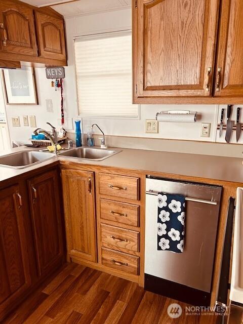 kitchen with brown cabinets, a sink, light countertops, dark wood finished floors, and stainless steel dishwasher