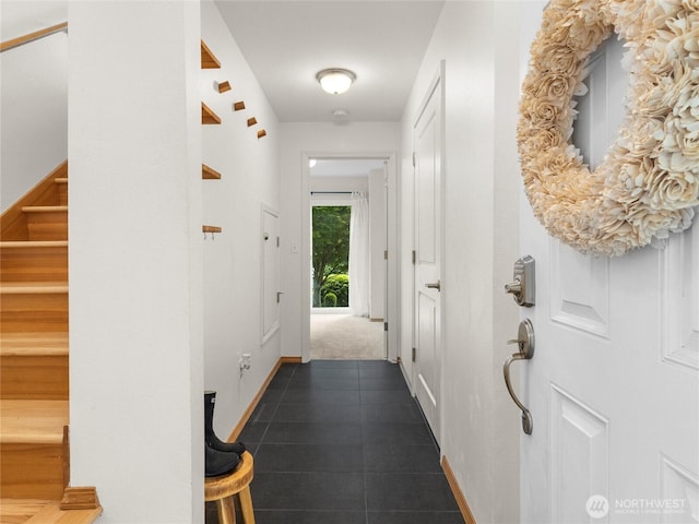hallway featuring baseboards, stairs, and dark tile patterned floors