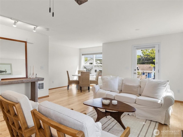 living room featuring light wood finished floors, rail lighting, healthy amount of natural light, and baseboards