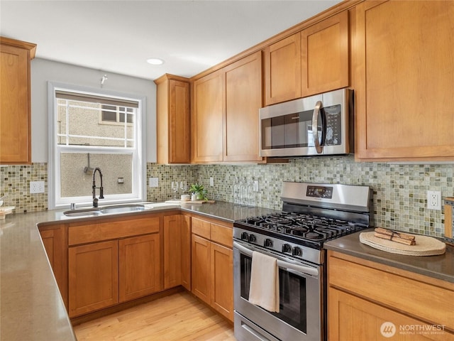 kitchen with stainless steel appliances, a sink, tasteful backsplash, brown cabinetry, and light wood-type flooring