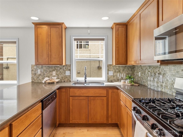 kitchen featuring appliances with stainless steel finishes, a sink, brown cabinetry, healthy amount of natural light, and recessed lighting