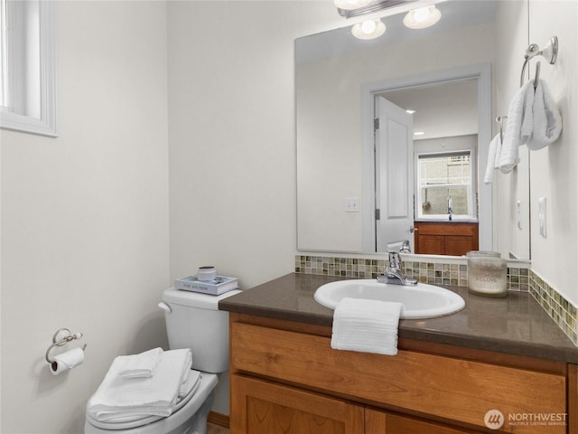 half bathroom featuring toilet, vanity, and backsplash