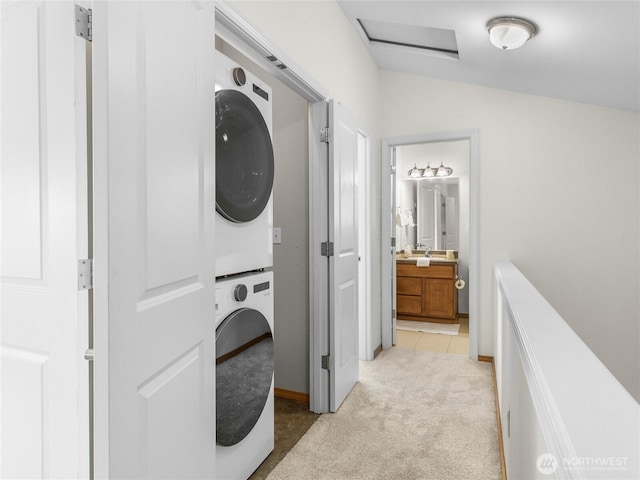 washroom featuring stacked washer / drying machine, light colored carpet, and baseboards