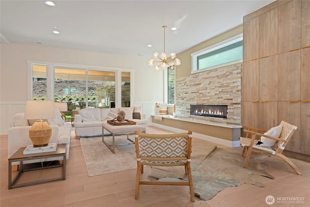living room featuring an inviting chandelier, wainscoting, a decorative wall, a fireplace, and light wood-type flooring