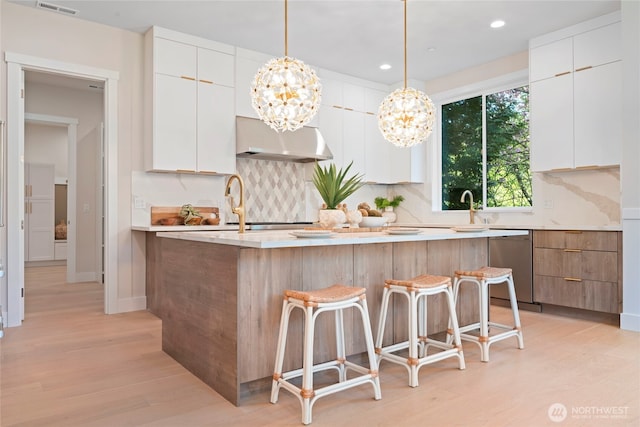 kitchen featuring decorative backsplash, dishwasher, light wood finished floors, an inviting chandelier, and under cabinet range hood