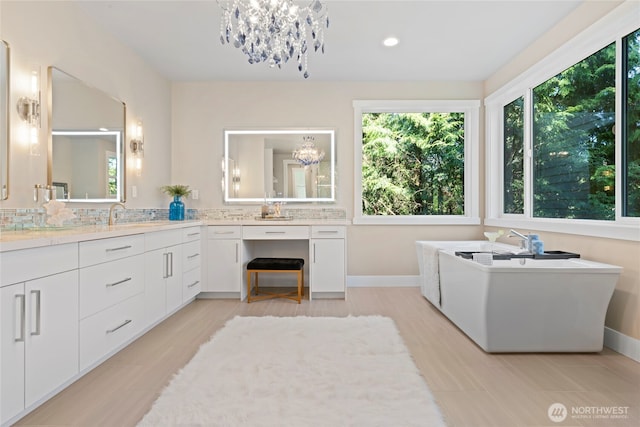 bathroom featuring vanity, a freestanding tub, baseboards, recessed lighting, and a notable chandelier