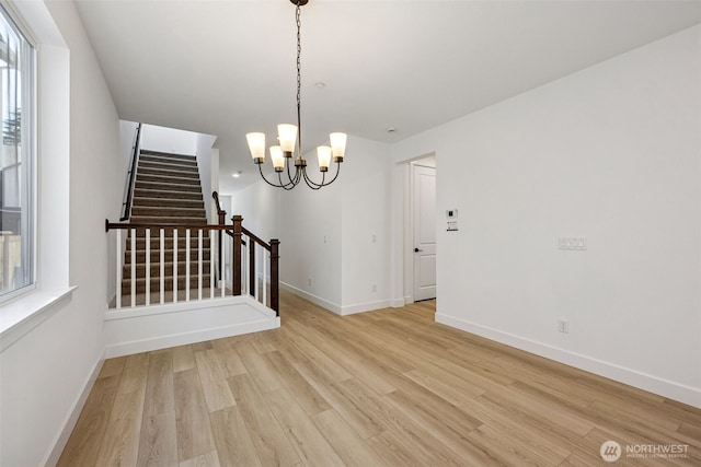 unfurnished dining area featuring stairs, baseboards, a chandelier, and light wood-style flooring