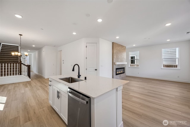 kitchen with stainless steel dishwasher, light wood-type flooring, white cabinetry, a tiled fireplace, and a sink