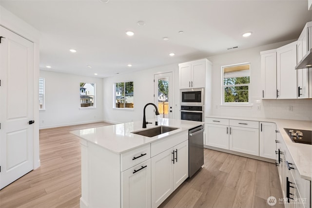 kitchen with light wood-type flooring, a sink, decorative backsplash, and appliances with stainless steel finishes