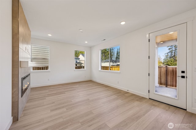 unfurnished living room featuring a tiled fireplace, recessed lighting, baseboards, and light wood finished floors