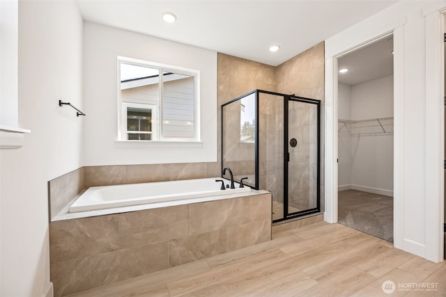 full bath with wood finished floors, recessed lighting, a bath, a spacious closet, and a stall shower