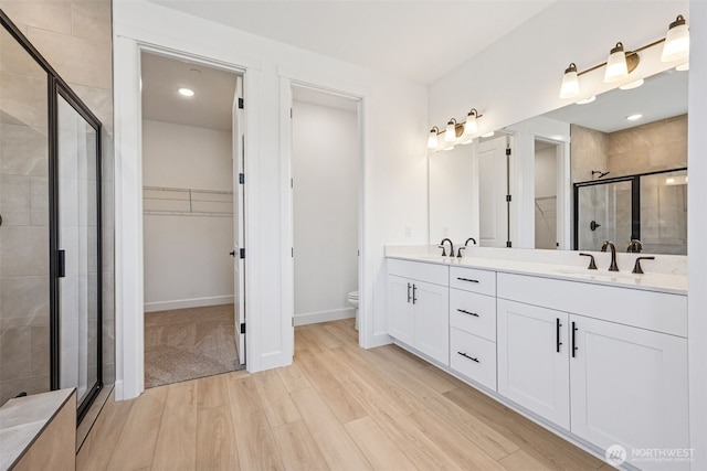 full bath with double vanity, wood finished floors, toilet, a sink, and a stall shower