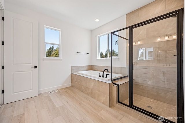 full bath featuring plenty of natural light, baseboards, a bath, and a shower stall