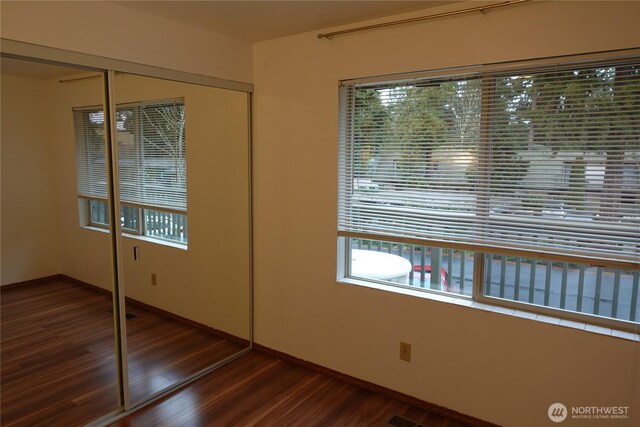 unfurnished bedroom featuring baseboards, wood finished floors, and a closet