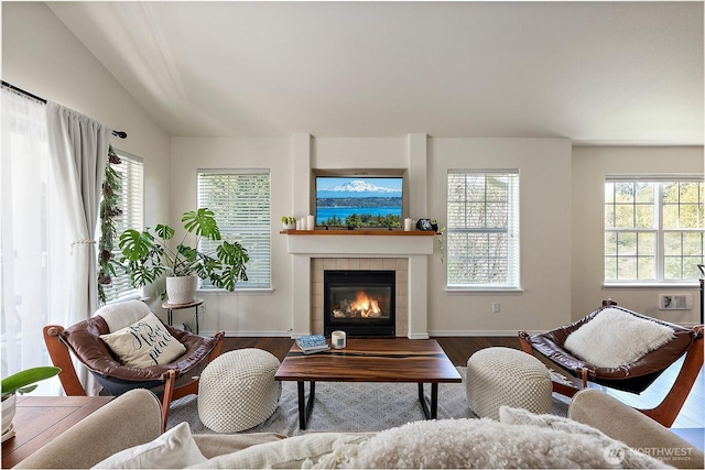 living area with baseboards, a tiled fireplace, wood finished floors, and lofted ceiling